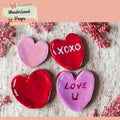 Heart-shaped cookies with 'XOXO' and 'I LOVE U' on a wooden surface with pink flowers.